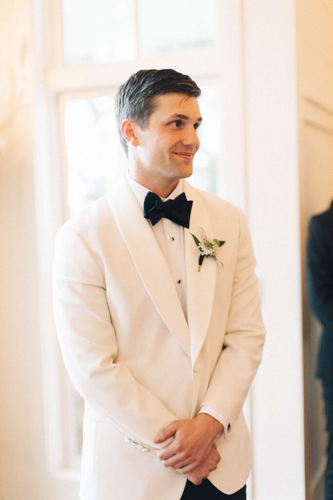 A groom smiles while anxiously waiting at the altar for his bride to enter