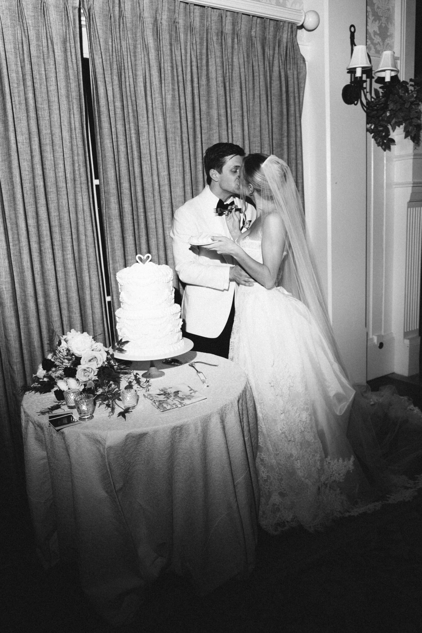 Newlyweds kiss after cutting the cake in black and white