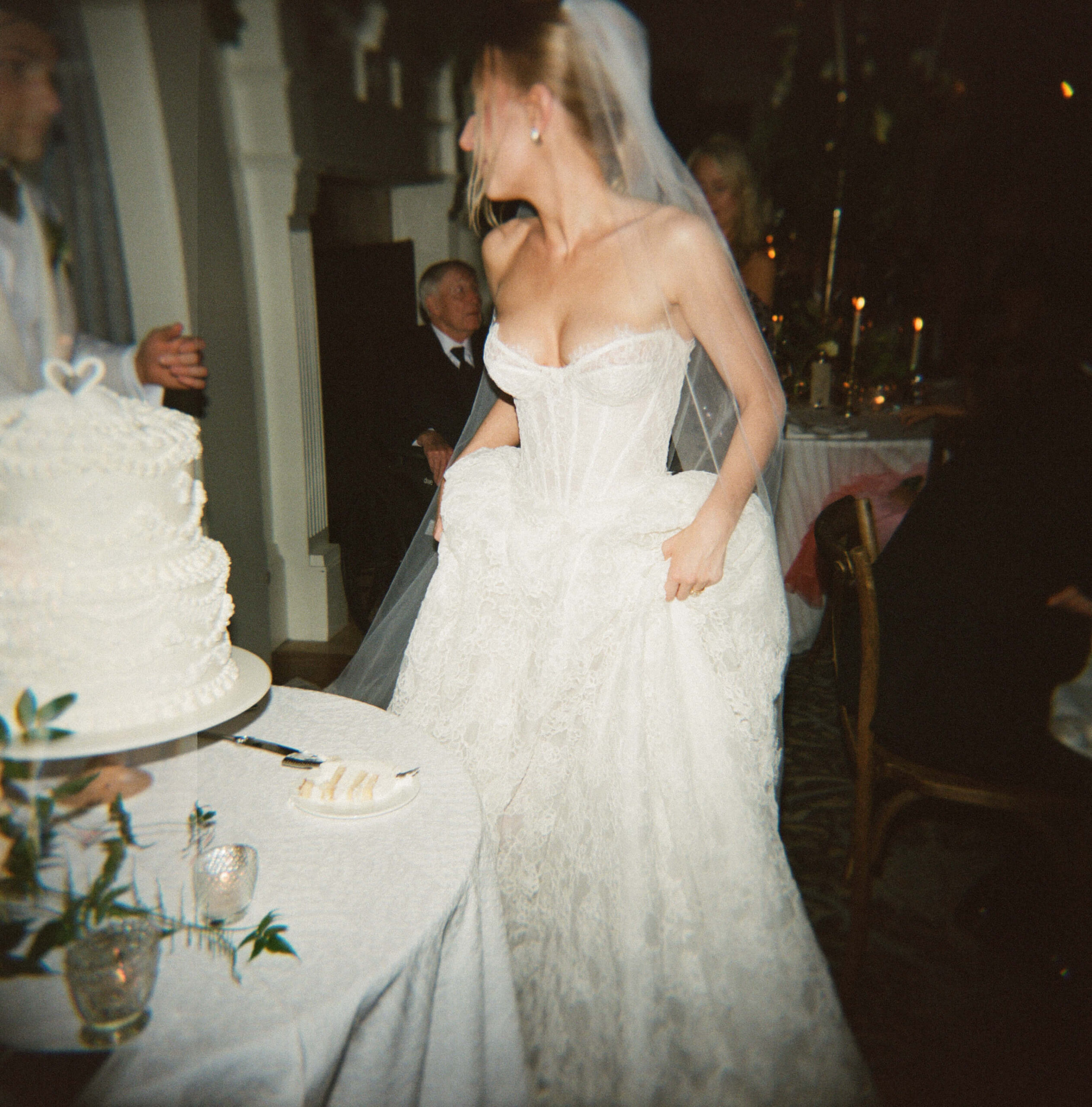 A bride hikes up her lace gown while in her reception by the cake and chatting with the groom
