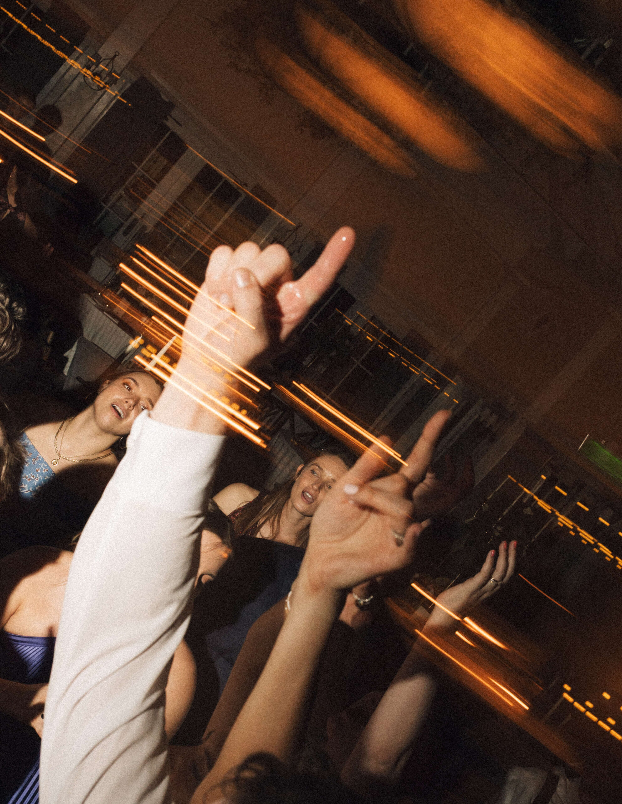 Wedding guests dance with fingers high in the air behind light streaks